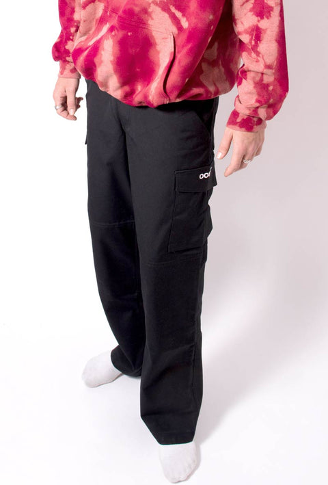 pantalone nero modello da lavoro in teflon con tasche sulle cosce e sul lato con stampato il logo taboo sulla tasca laterale. Dettaglio indossato insieme ad una felpa rossa con effetto tie dye