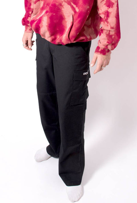  pantalone nero modello da lavoro in teflon con tasche sulle cosce e sul lato con stampato il logo taboo sulla tasca laterale. Dettaglio indossato insieme ad una felpa rossa con effetto tie dye