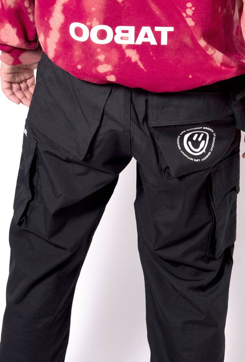 pantalone nero modello da lavoro in teflon con tasche sulle cosce e sul lato con stampato il logo taboo sulla tasca laterale. Dettaglio retro indossato con felpa tie dye rossa